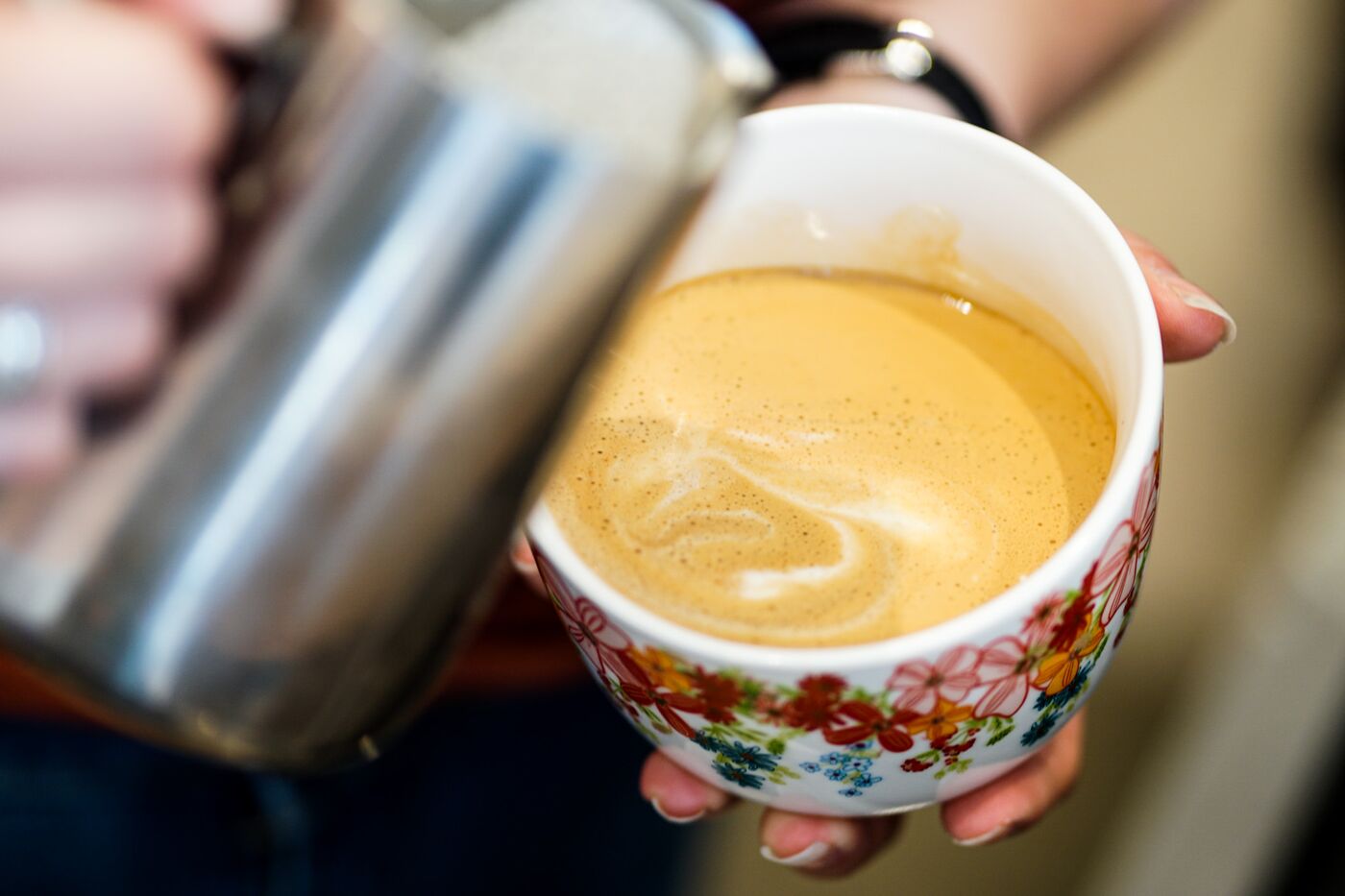 Latte being poured into a floral cup at Hilltop Coffee